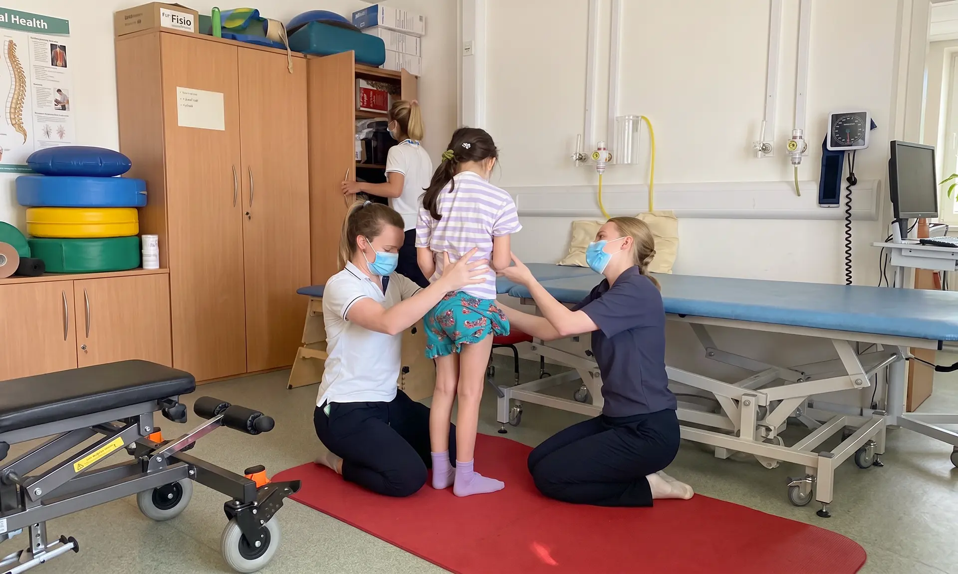 A physiotherapist treating a young patient with a colleague in a clinic room